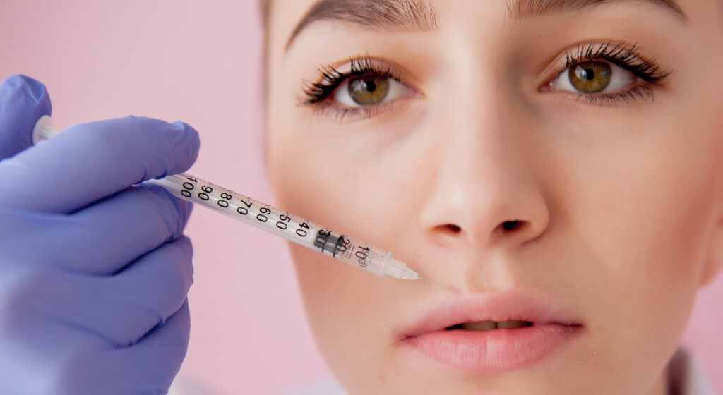 Doctor-in-gloves-giving-woman-botox-injections-in-lips-on-pink-background.-1024x560